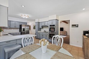 A modern kitchen with grey cabinets, stainless steel appliances, and a dining area with a white table and chairs. - 5BR Near Graceland Sleeps 10 with Piano, Fire Pit, and Games (Memphis)