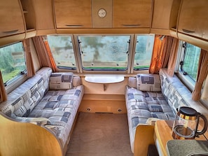 L’intérieur d’un camping-car est aménagé avec deux espaces salon, une table centrale et une fenêtre offrant une vue sur l’extérieur.