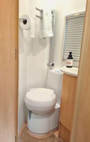 Un baño pequeño con inodoro, toallero, rollo de papel higiénico y lavamanos con jabón.