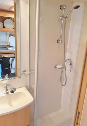 A bathroom with a shower, sink, and mirror. - Sunshine Caravan - Private & Self-Contained, 250m from Hospital (Tauranga)