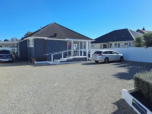 A residential property with a gravel driveway, a white car parked in the driveway, and a small building with a porch.