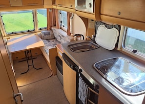 Une cuisine compacte pour camping-car, équipée d’un évier, d’une cuisinière et d’un petit coin repas.