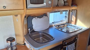 A compact kitchenette with a microwave, sink, stove, and storage shelves.