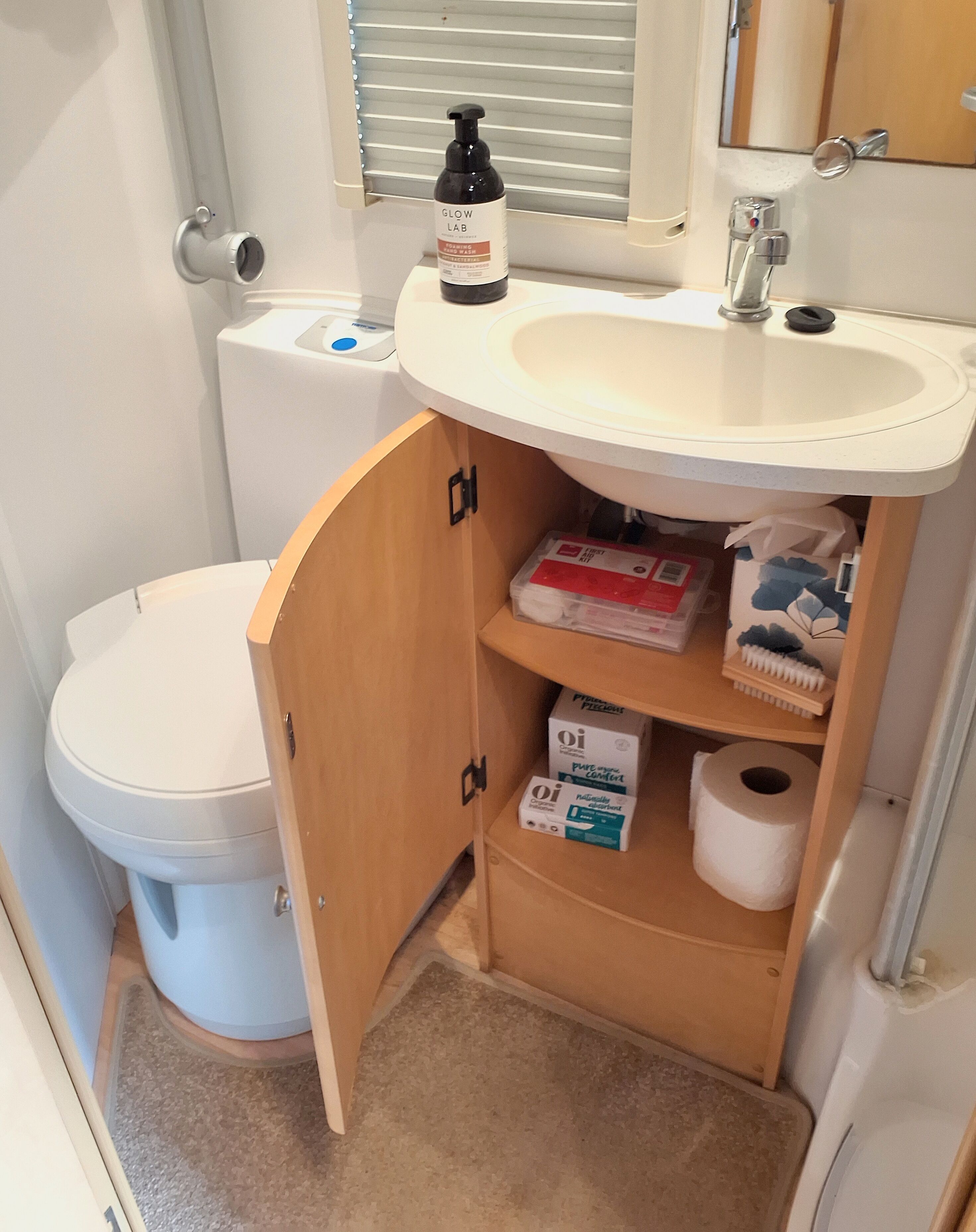 A compact bathroom with a toilet, a sink, and a cabinet containing toiletries.