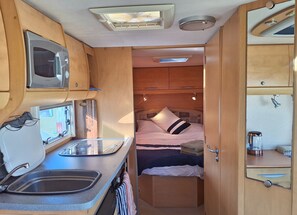 A compact RV interior with a kitchenette, a bed, and a small bathroom.
