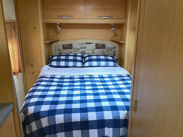 A narrow room with a bed, wooden cabinets, and a small shelf.
