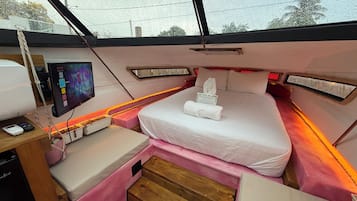 Una habitación compacta con una cama, un escritorio pequeño con una computadora y una ventana con vista a árboles.
