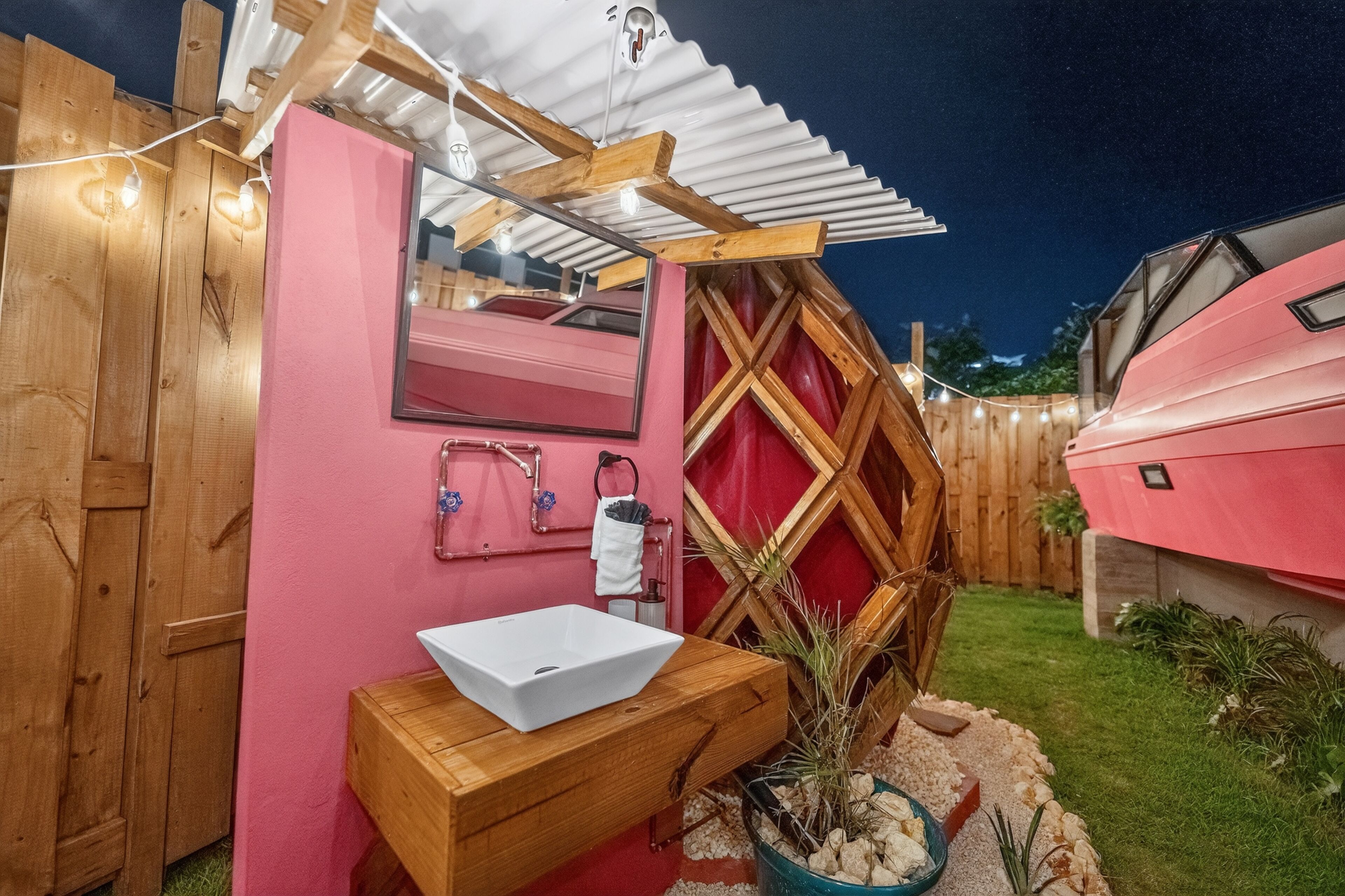 A compact outdoor bathroom with a wooden vanity, a white sink, and a mirror.
