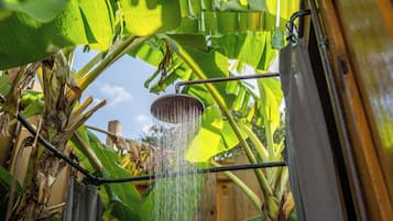 A showerhead with water flowing, surrounded by banana leaves and a wooden fence.