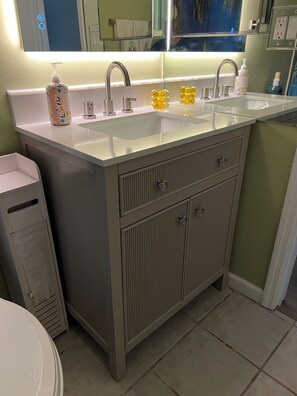 Ein Badezimmer mit einem Doppelwaschbecken, einem Spiegel und einer Toilette.