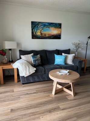Ein modernes Wohnzimmer mit einem grauen Sofa, einem runden Couchtisch aus Holz und einem an der Wand hängenden abstrakten Gemälde.