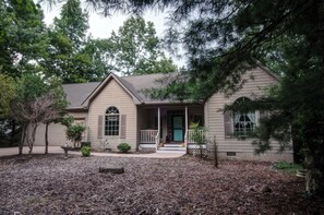 A single-story house with a front porch, a small front yard with mulch, and a statue. - Spacious 4-bedroom house with AC in amazing Brevard CONNESTEE FALLS (Brevard)