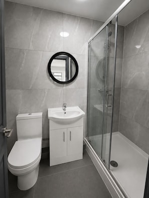 Et moderne badeværelse med toilet, vask og brusekabine i glas.