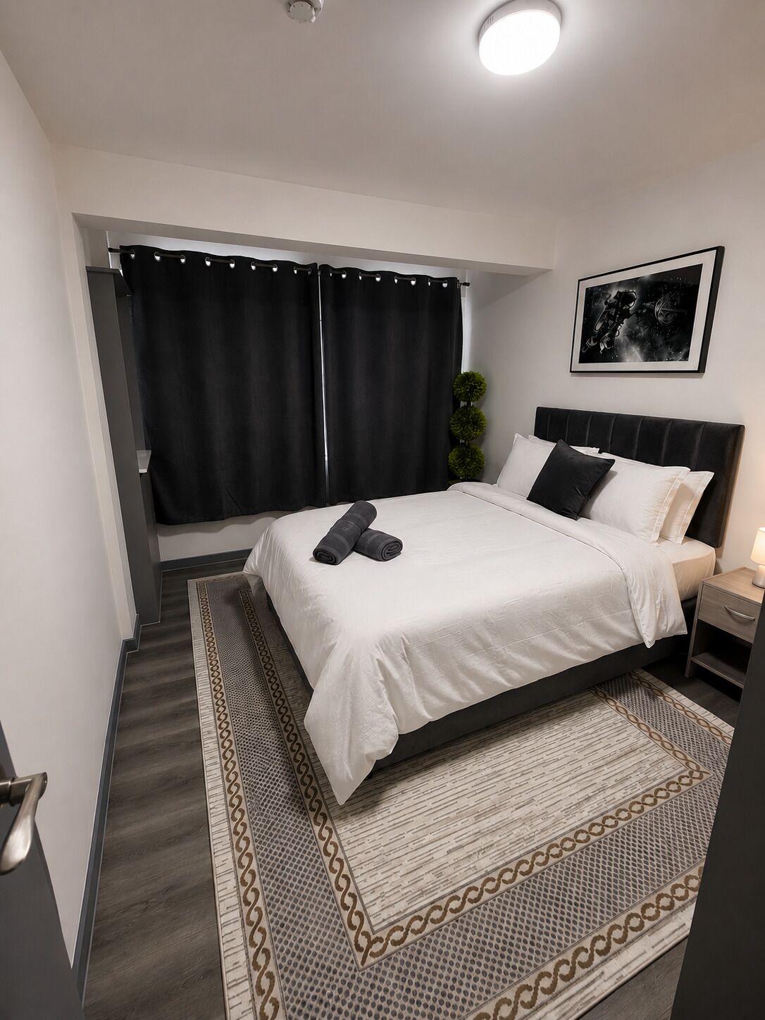 Une chambre moderne avec un grand lit, une table de chevet, une lampe fixée au mur et un tableau encadré.