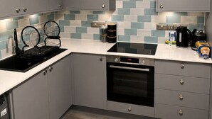 Et moderne køkken med lysegrå skabe, en sort komfur og en flisebeklædt bagvæg.