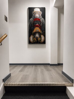 Un pasillo con una escalera, una obra de arte enmarcada en la pared y suelo de madera.