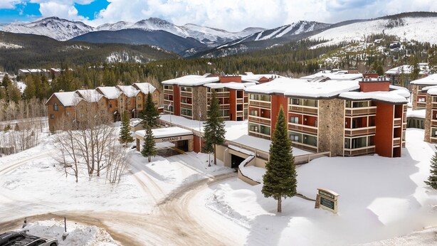A snow-covered building with a ski resort in the background. - Ski Retreat Condo w/ Pool, Hot Tub & Balconies (Winter Park)