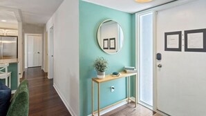 Un couloir avec un mur de couleur turquoise, un miroir rond, une console sur laquelle est posée une plante, et une porte blanche ornée de deux avis.