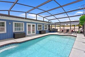 Ein überdachter Swimmingpool mit klarem, blauem Wasser, eine Pergola mit Lichterketten und eine Terrassenanlage mit Liegestühlen.