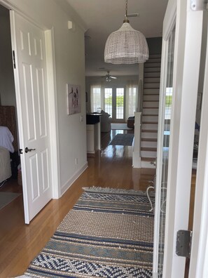 Un pasillo con un tapete estampado, una puerta blanca, un ventilador de techo y una escalera que sube a un nivel superior.