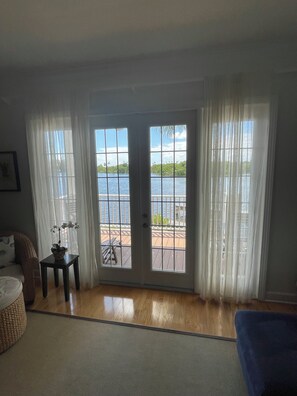 Una habitación con vista a un cuerpo de agua a través de un ventanal, una silla de mimbre, una mesita con una planta y una silla azul.