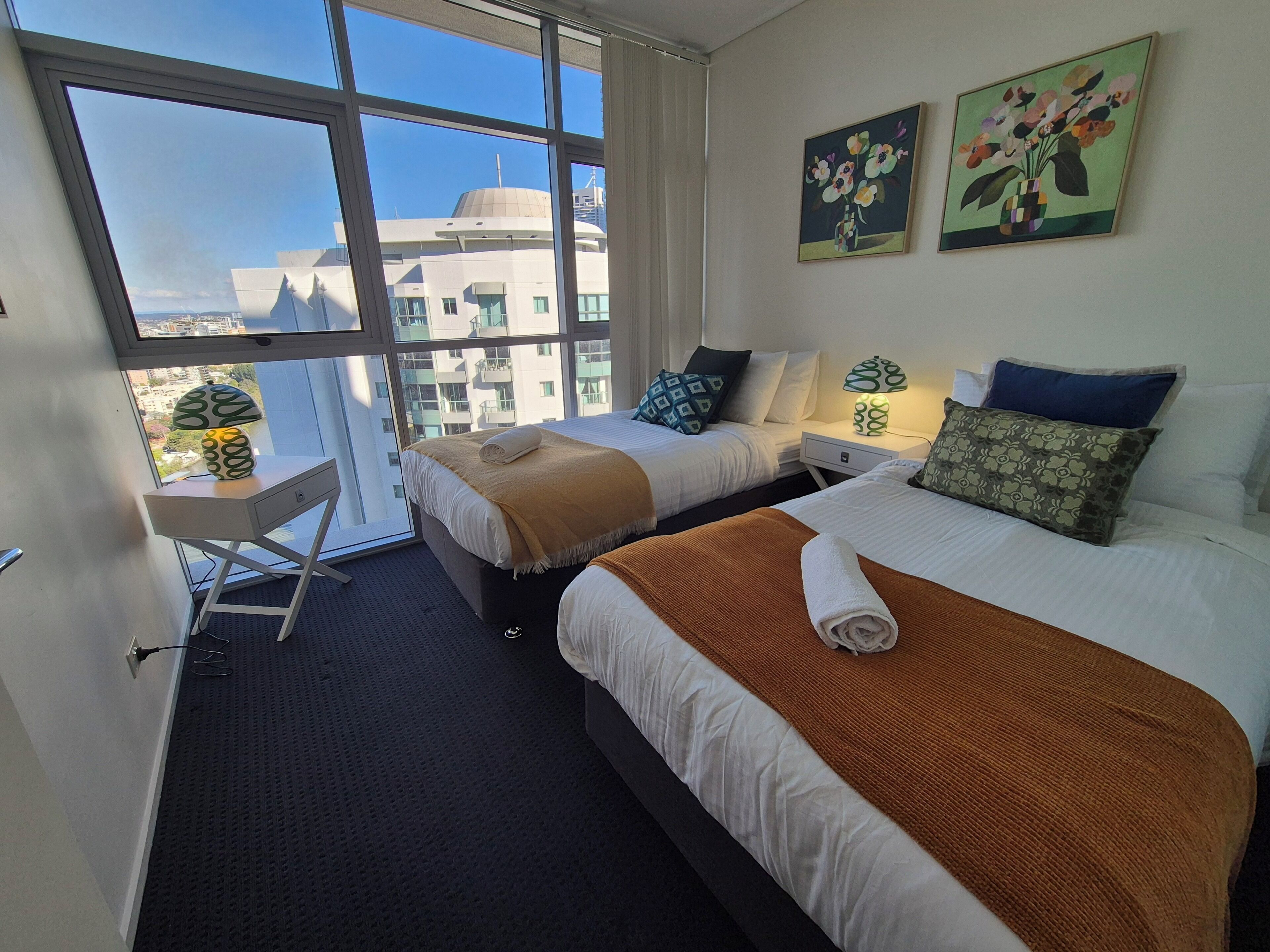 A hotel room with two beds, a desk, and a large window offering a city view.