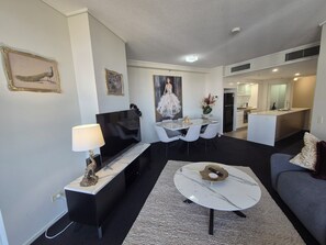 A modern living room with a flat-screen TV, a dining table with chairs, a sofa, and a kitchen area in the background. - The Gilded Gallery I Art-Inspired Luxe (Brisbane City)