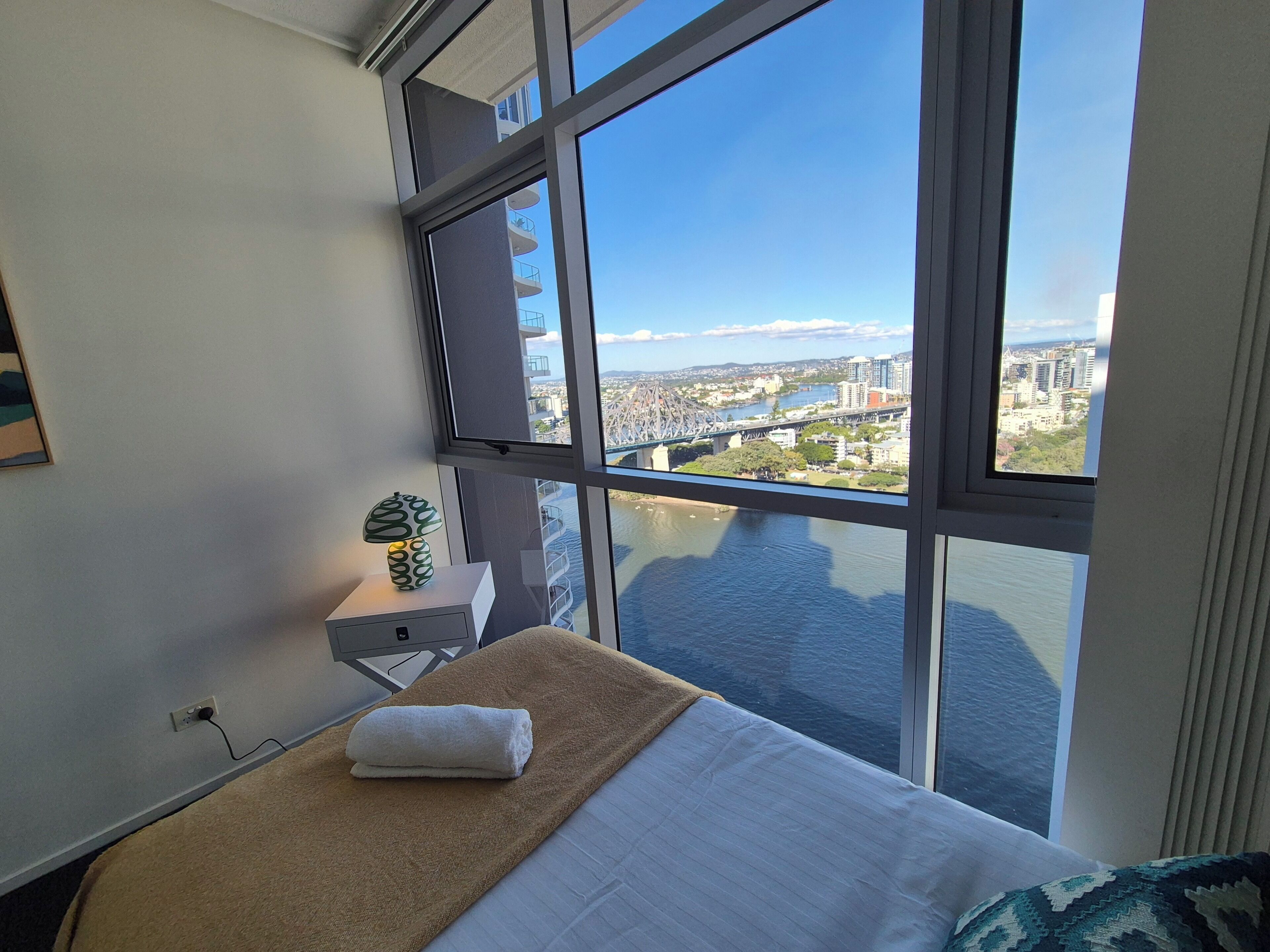 A hotel room with a large window, a bed with a towel, a nightstand, and a lamp.