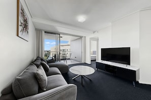 A modern hotel room with a sofa, a flat-screen TV, a small round table, and a balcony with a view. - The Gilded Gallery I Art-Inspired Luxe (Brisbane City)