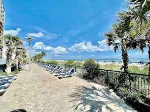 A paved walkway with sun loungers, a railing, and palm trees. - Salty Vibes Sleeps 4 315 (Myrtle Beach)