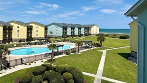 A hotel with a swimming pool, a beach view, and a well-maintained lawn.