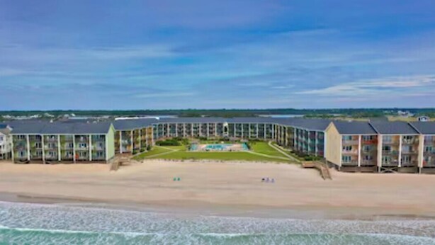 A beachfront hotel with multiple buildings, a swimming pool, and a sandy beach.