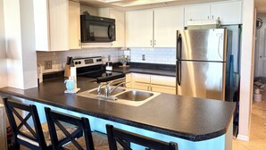 A modern kitchen with white cabinets, a stainless steel refrigerator, a black microwave, and a granite countertop.