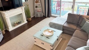 A living room with a fireplace, a television, a sofa, a coffee table, and a view of an outdoor deck.