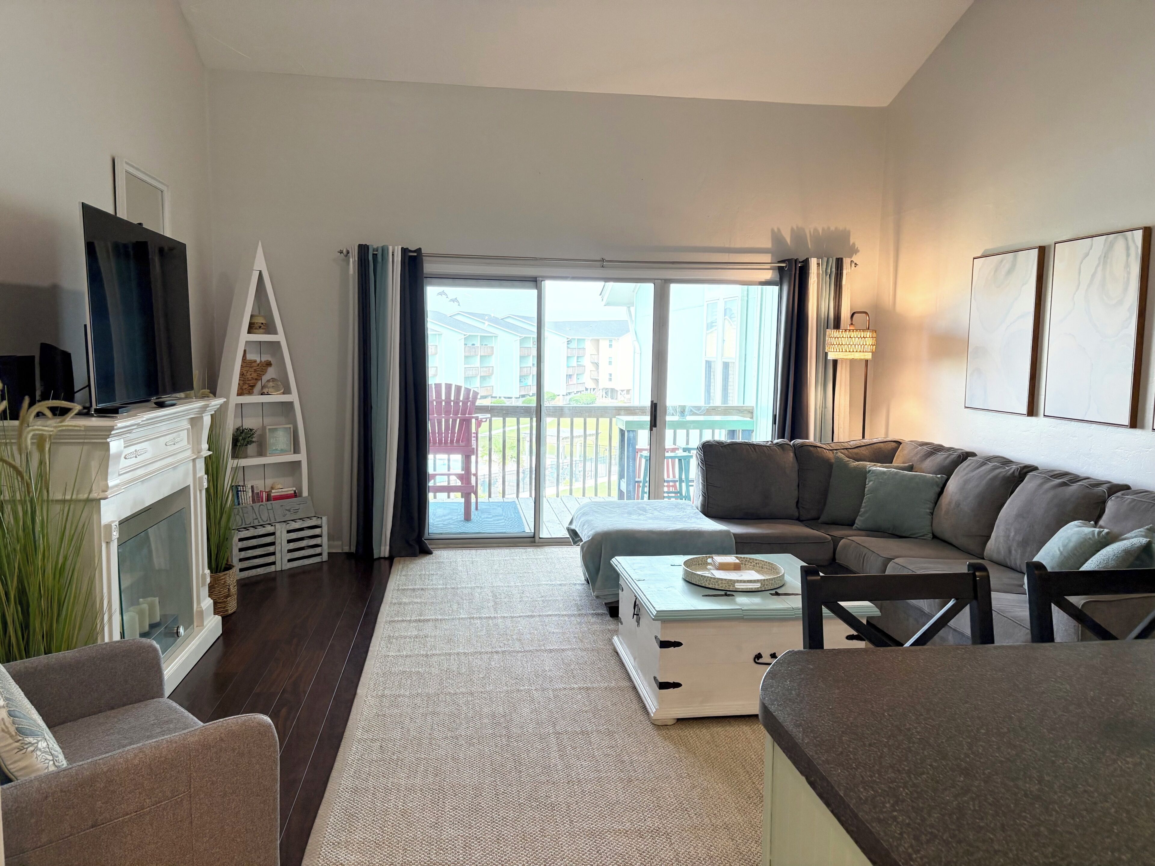 A living room with a sofa, a television, a fireplace, a balcony with a chair, and a large window.
