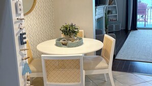 A dining area with a round table, two chairs, a hanging light fixture, a mirror, and a wall with a herringbone pattern.