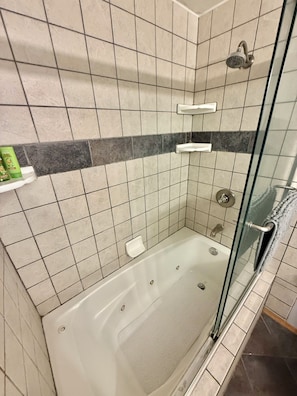 A glass-enclosed shower stall with a bathtub, tiled walls, and a soap dish.