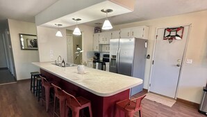 Uma cozinha moderna com ilha central, banquetas, eletrodomésticos de aço inoxidável e iluminação pendente.