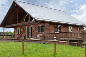 Eine Holzhütte mit großer Veranda, einer überdachten Terrasse und einem eingezäunten Rasenstück.