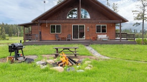 En stuga byggd av trä med en inglasad veranda, en grill och en eldstad.