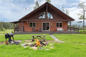Eine Holzhütte mit überdachter Veranda, Grill und Feuerstelle.