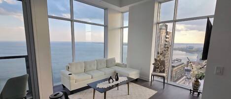 Ein modernes Wohnzimmer mit einem weißen Sofa, einem Couchtisch und Blick auf das Meer und die Stadt durch große Fenster.