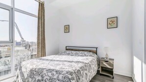Un dormitori amb un llit, una tauleta de nit, una finestra amb cortines i dos quadres a la paret.