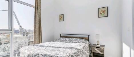 Un dormitorio con cama, mesita de noche, ventana con cortinas y dos cuadros en la pared.
