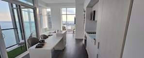 Ett modernt rum med ett långt bord, stolar, en soffa och utsikt över vattnet.