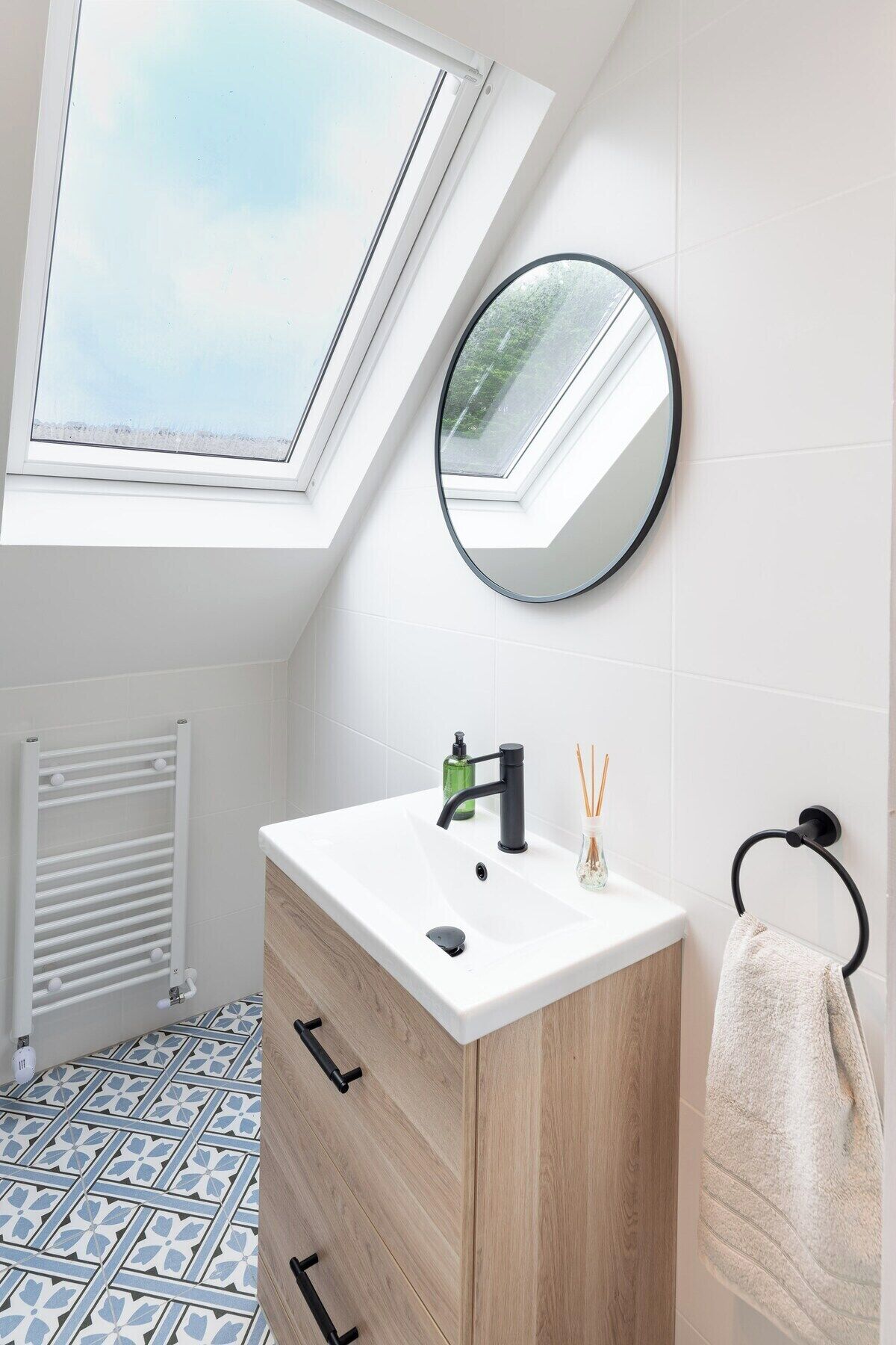 A modern bathroom with a skylight, a round mirror, a white sink, and a towel rack.