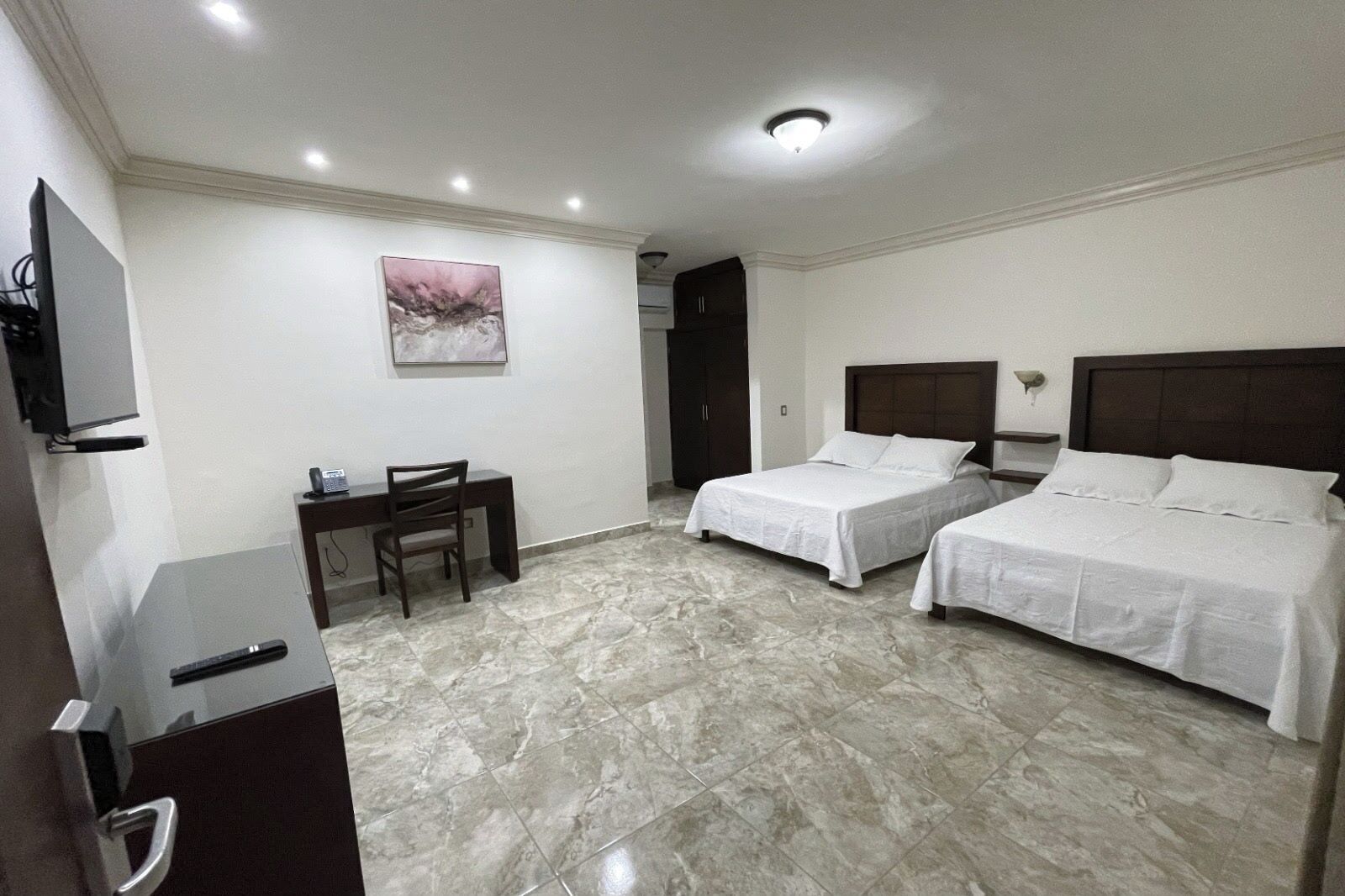 Habitación de hotel con dos camas, un escritorio, una silla, un televisor y un cuadro en la pared.