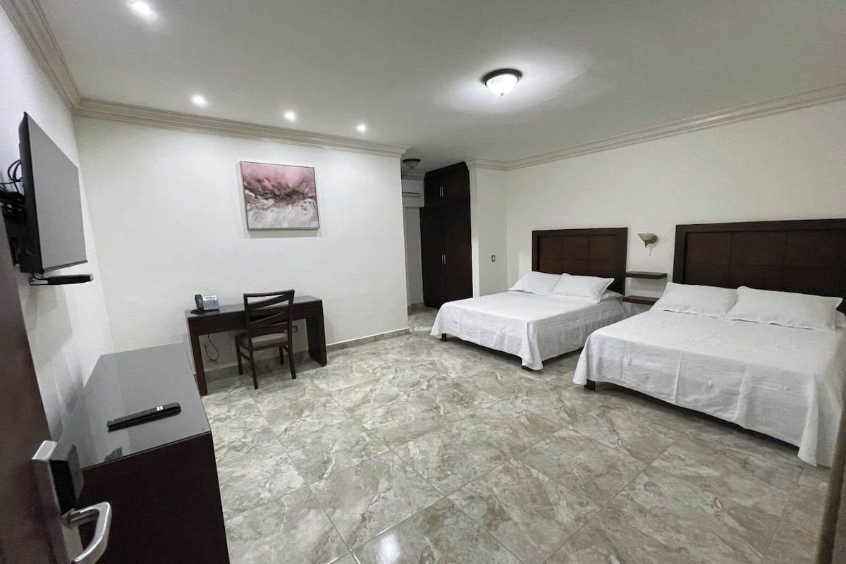 A hotel room with two beds, a desk, a chair, a television, and a painting on the wall.