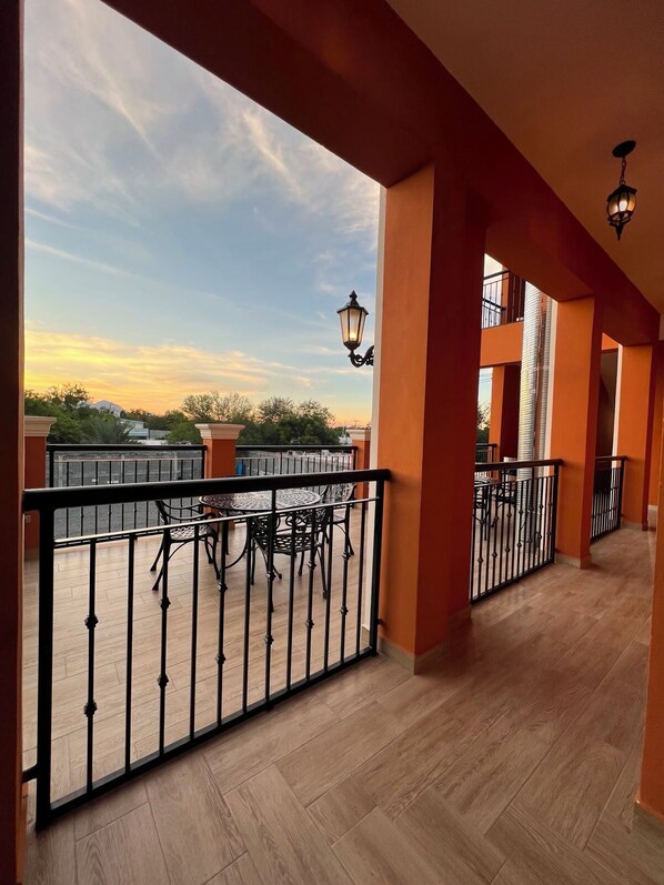 A balcony with a view of the sky, a table with chairs, and a railing.