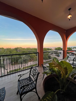 A balcony with a view of the sunset, a potted plant, and a metal chair.